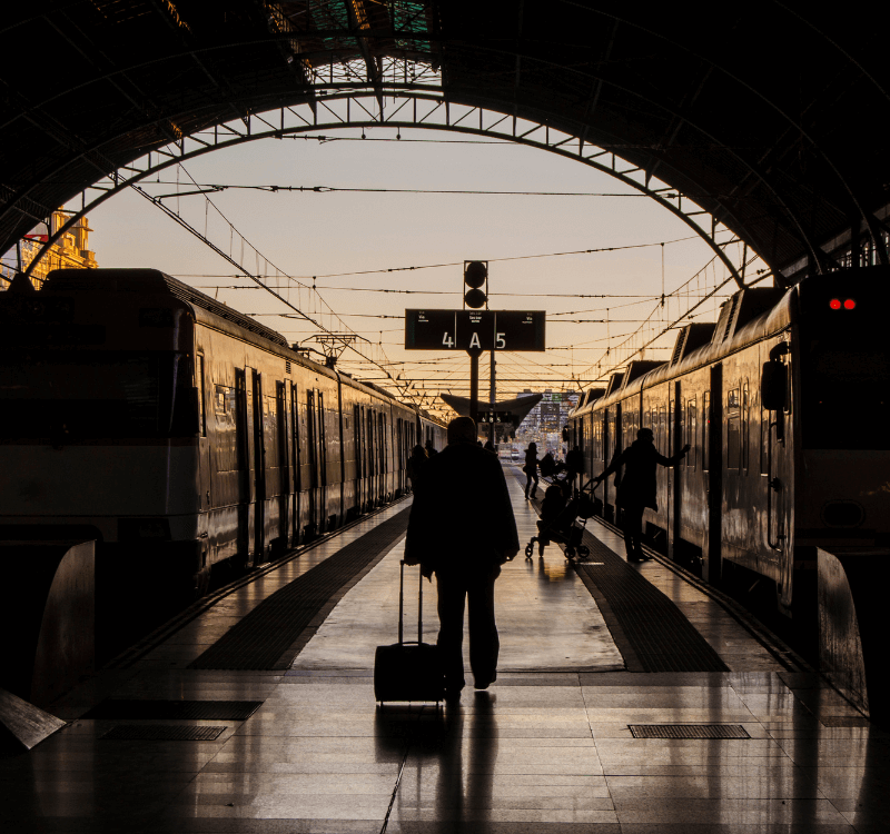 Tren Travesía por España Hombre visto desde atrás en una estación de tren por la noche jalando una maleta de mano